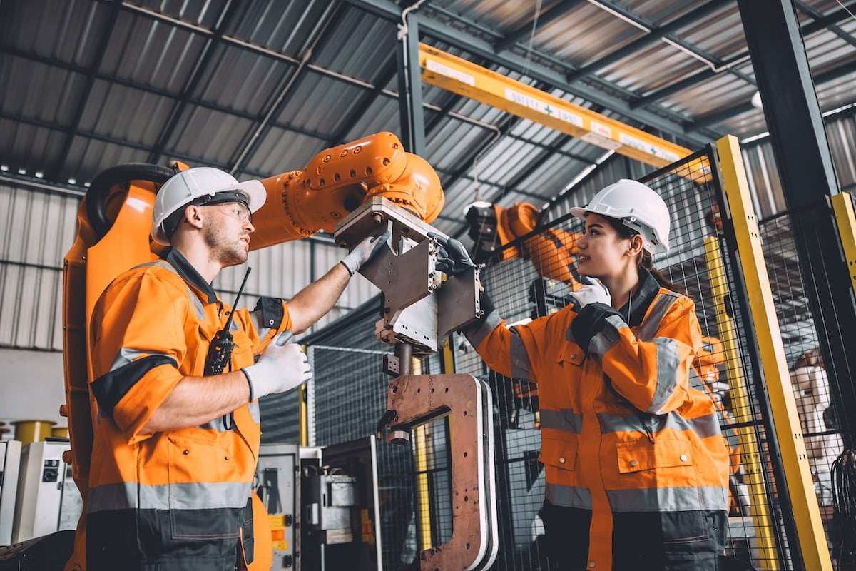 Techniciens en tenue de sécurité inspectant un bras robotisé dans un atelier industriel, dans le cadre d’une démarche de prévention des risques PAPRIPACT