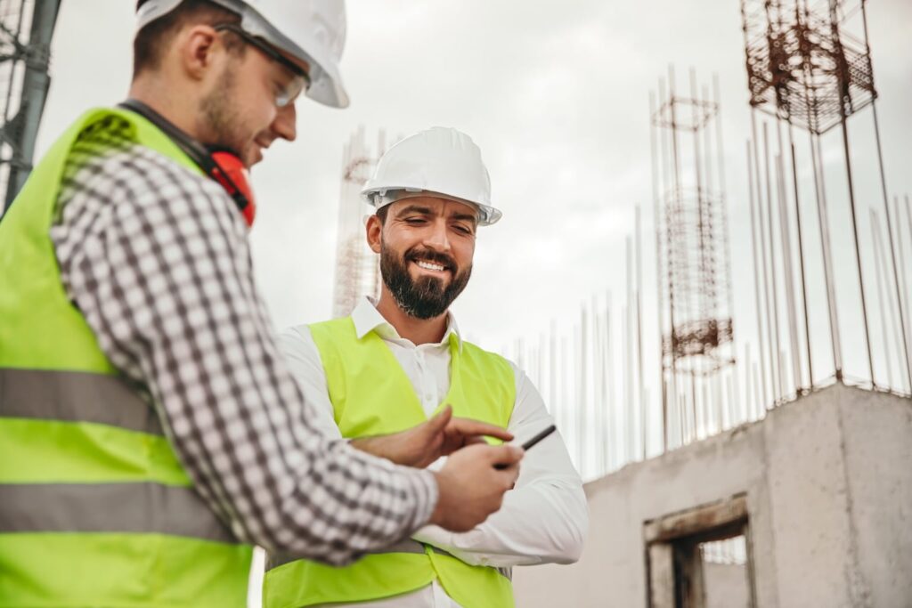 Deux professionnels du bâtiment en gilet et casque de sécurité consultent un Document Unique (DUERP) sur chantier, illustrant la mise en œuvre d’une démarche de prévention.